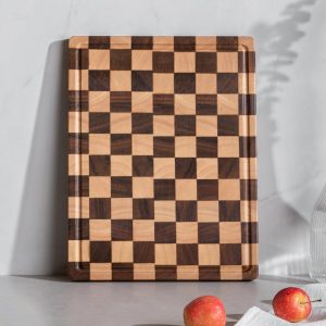 Upright checkerboard-pattern end grain wood cutting board with perimeter juice groove on a white and gray background