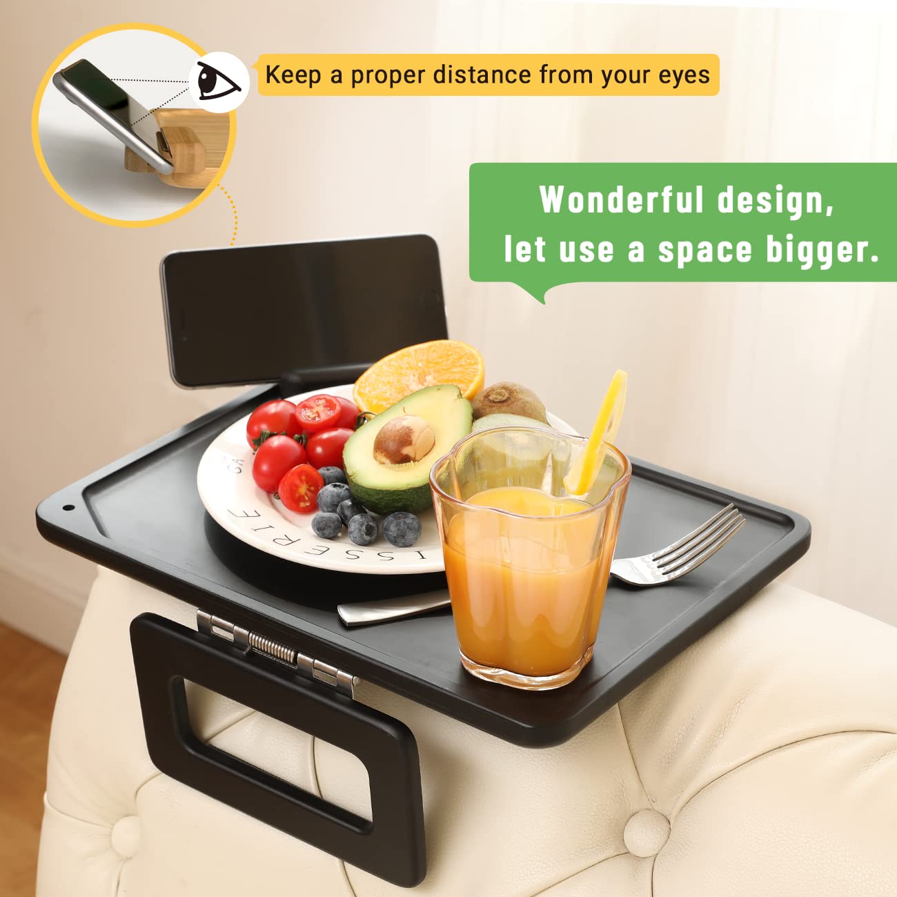 Black couch arm tray holding fruit, orange juice and a phone on an upholstered sofa arm