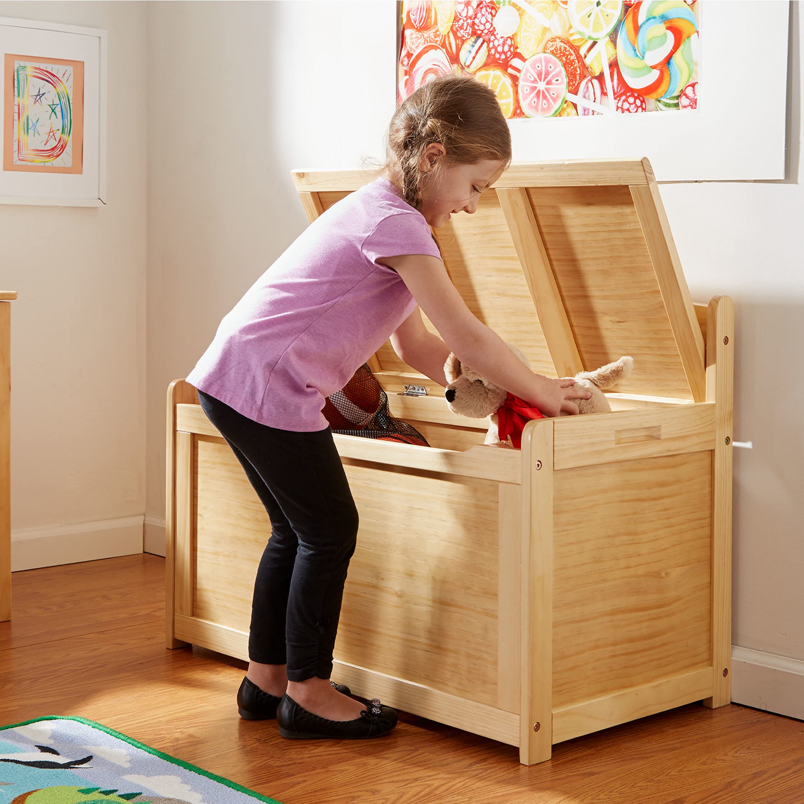 Child placing a stuffed toy into a wooden toy chest with the lid raised