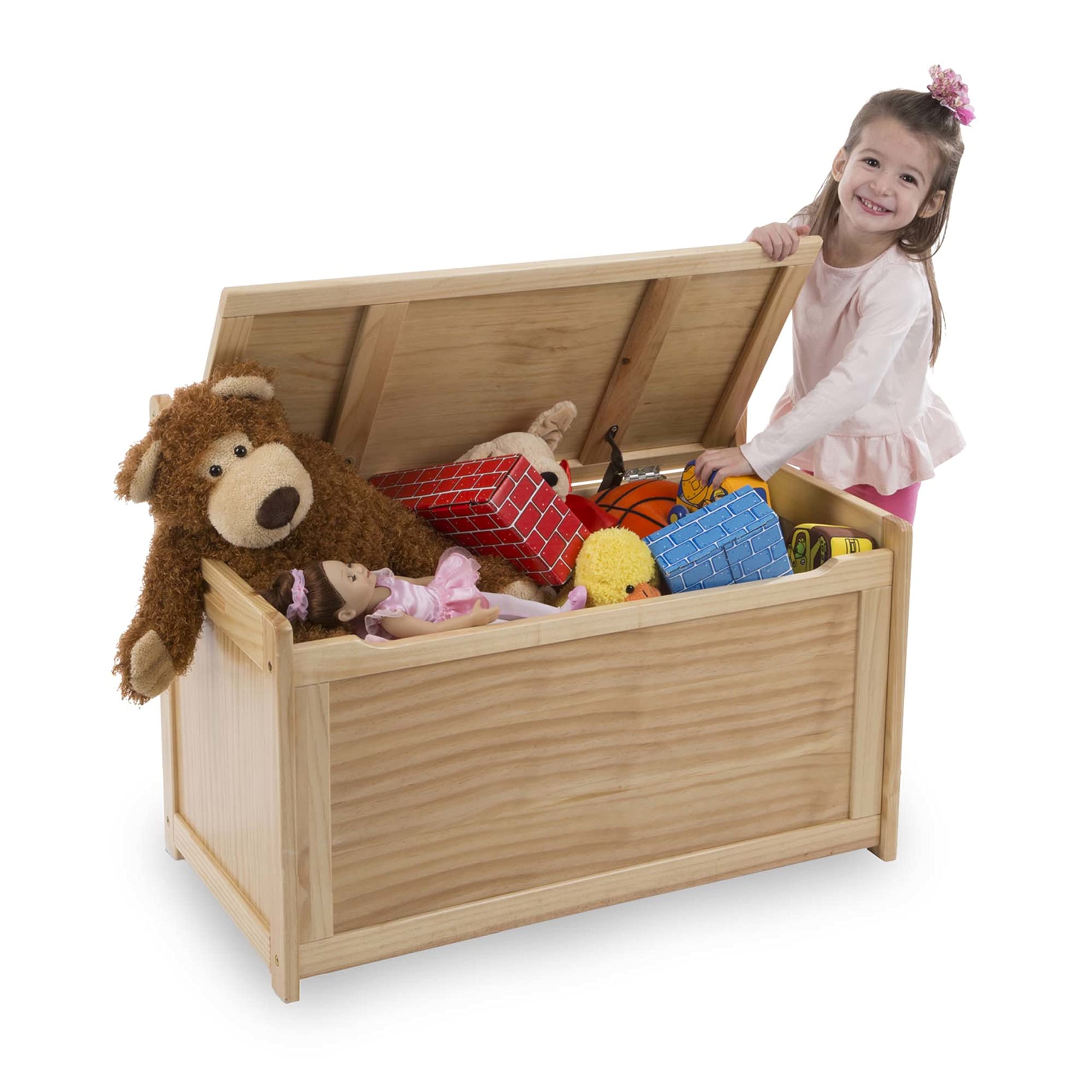 Open wooden toy chest holding stuffed toys, a ball and blocks with a child standing behind it