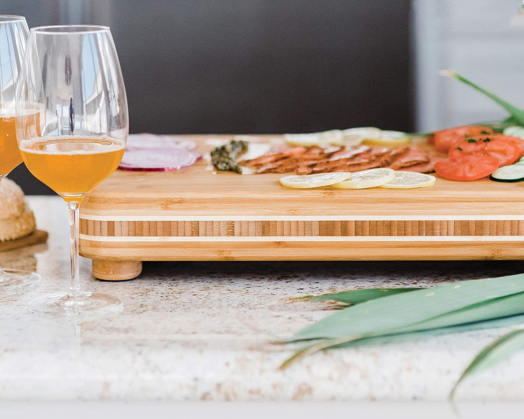 Bamboo chopping board staged with sliced food on a table beside drinking glasses