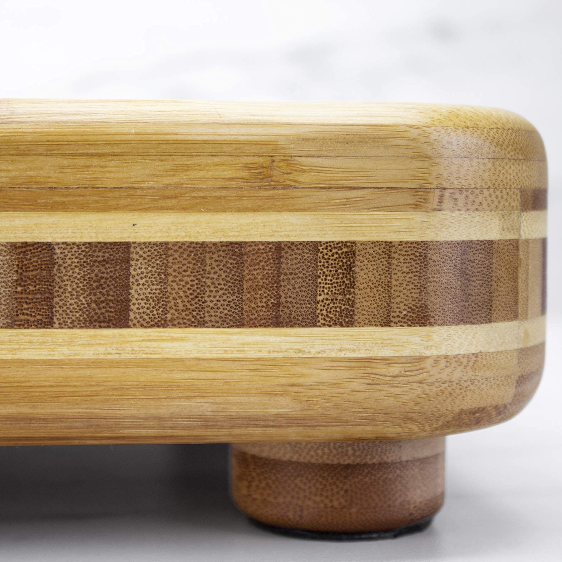 Close-up of the bamboo board's layered side band, rounded corner and round foot with a dark bottom pad