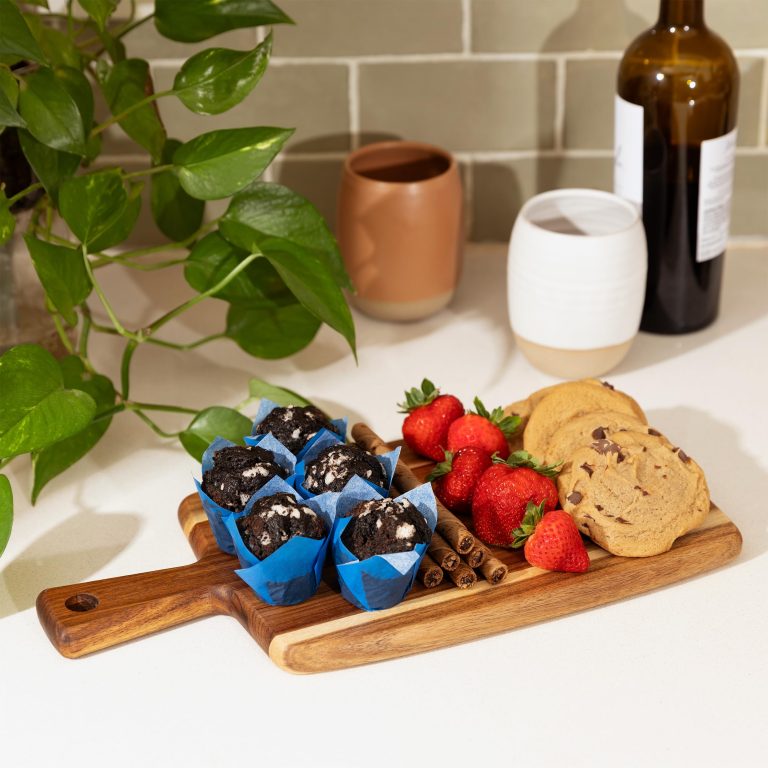 Handled wood board arranged with strawberries, cookies and small baked goods on a kitchen counter
