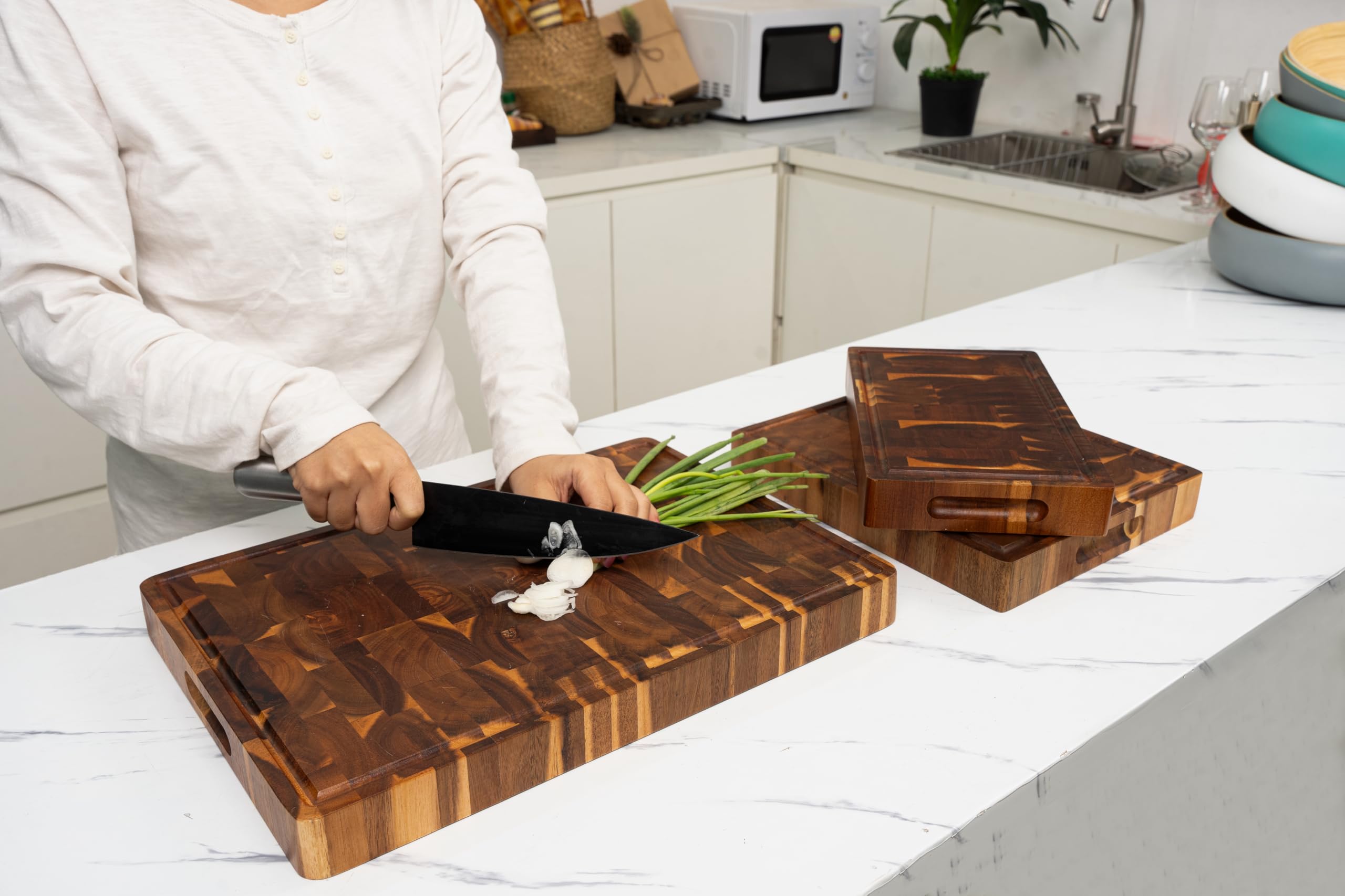 Wood cutting board set shown with scallions being sliced on a large board and two smaller boards behind it