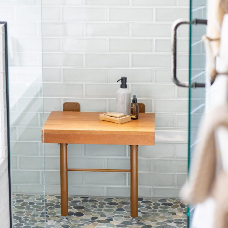 Wooden folding shower seat shown open in a tiled shower with two front legs and rear wall plates