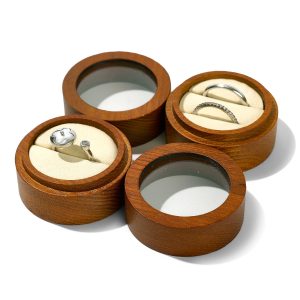 Round ring box with clear lid and cream slotted inserts, shown open with rings