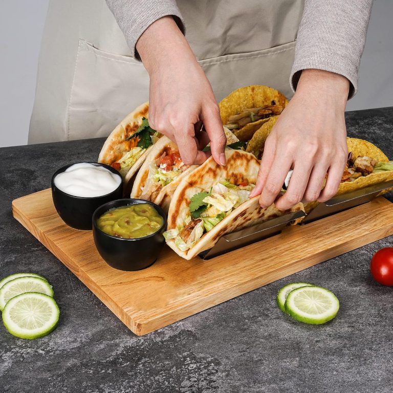 Hands arranging tacos in metal racks on a wooden serving tray beside two black dip bowls