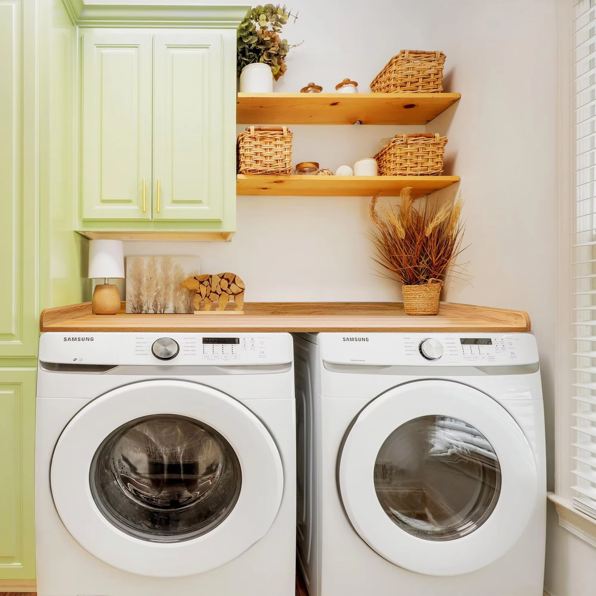 Wood-toned laundry countertop spanning two white front-loading appliances beneath green cabinets and wall shelves