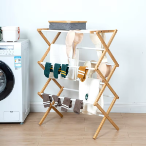 Laundry drying rack with a wood-toned crossed frame and white rods, pictured with socks and clothing beside a washing machine