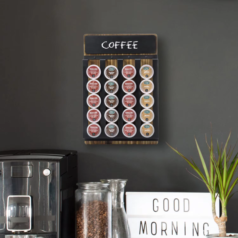 Wall-mounted coffee pod organizer with a wood-toned back, four black vertical channels and a top chalkboard, pictured above a coffee station