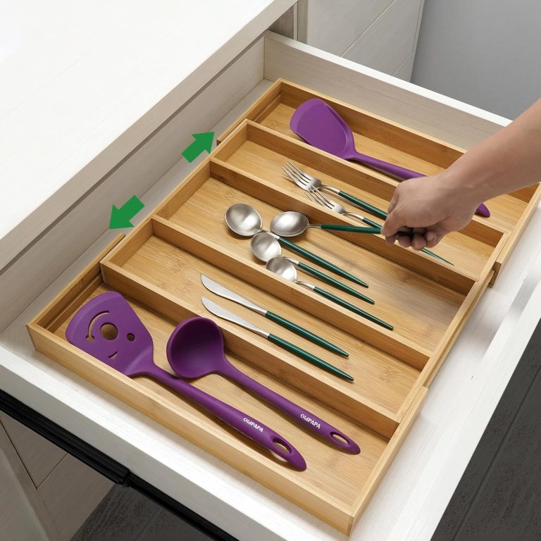 Hand reaching for a fork in an expandable bamboo cutlery tray holding spoons, knives and purple serving utensils in a drawer