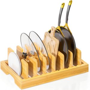 Bamboo pot lid organizer holding glass lids, frying pans, a cutting board and a plate between upright dividers