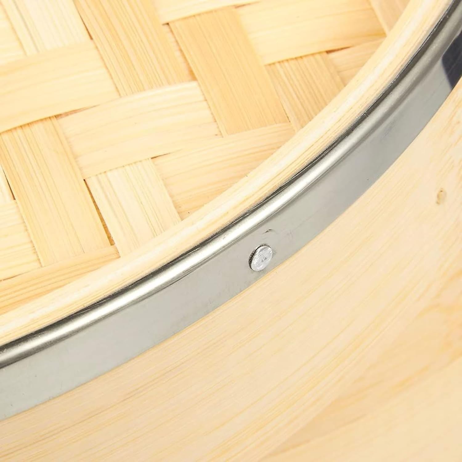 Close-up of a metal reinforcing ring and fastener beside the woven bamboo lid and steamer rim