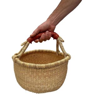 Hand holding a round handwoven grass basket by its brown leather-wrapped carrying grip
