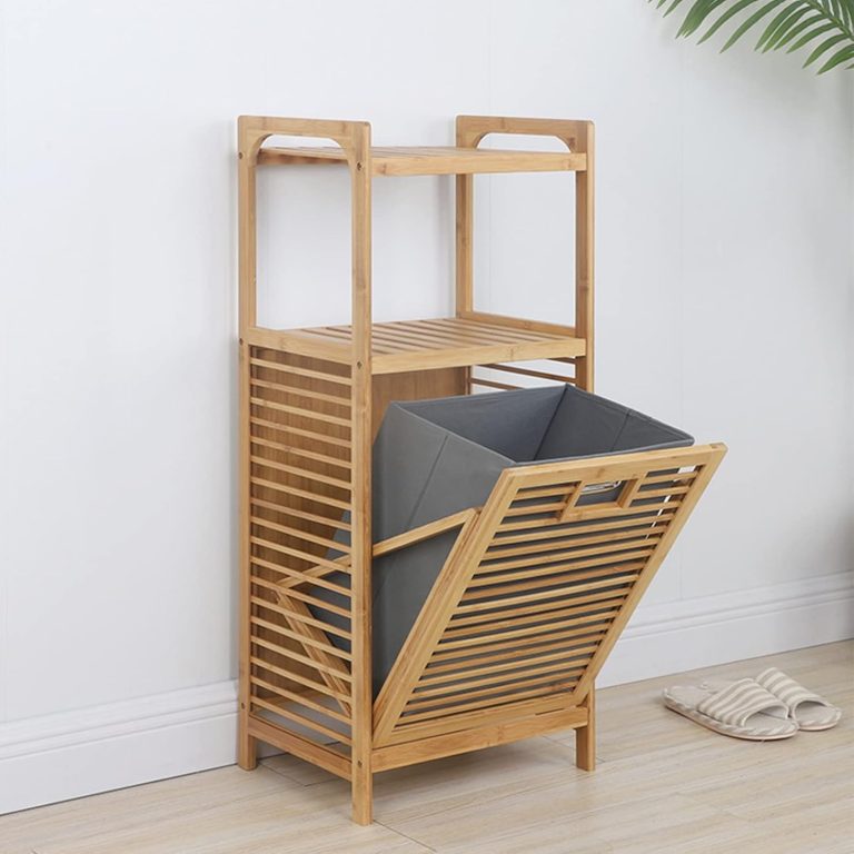 Bamboo laundry organizer with two upper slatted shelves, a plain cutout front handle and an empty gray fabric bin tilted forward beside a wall