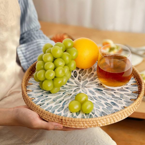 Round rattan tray with blue leaf inlay held beneath grapes, an orange and a glass of tea
