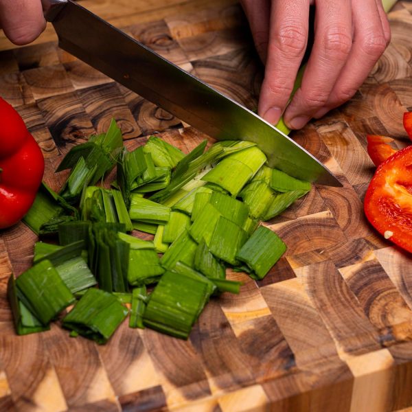 Close view of vegetables being sliced on the block-pattern surface of an acacia wood cutting board