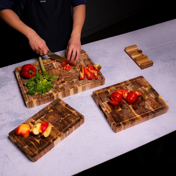 Large, medium and small acacia wood cutting boards arranged on a kitchen worktop with vegetables and fruit