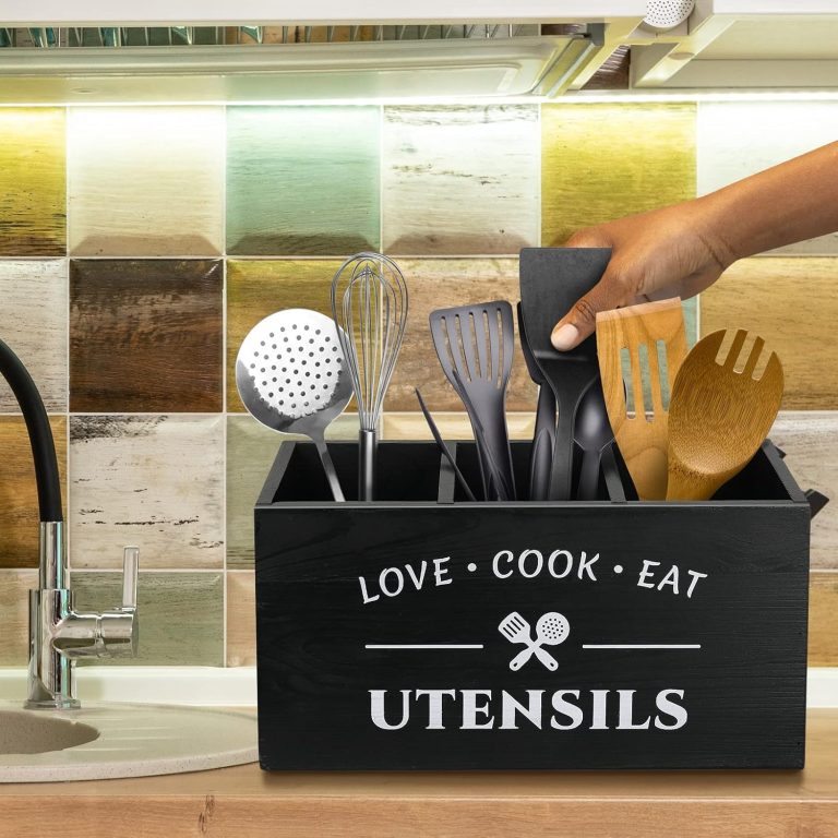 Three-compartment black utensil holder on a kitchen countertop with a hand selecting a cooking tool