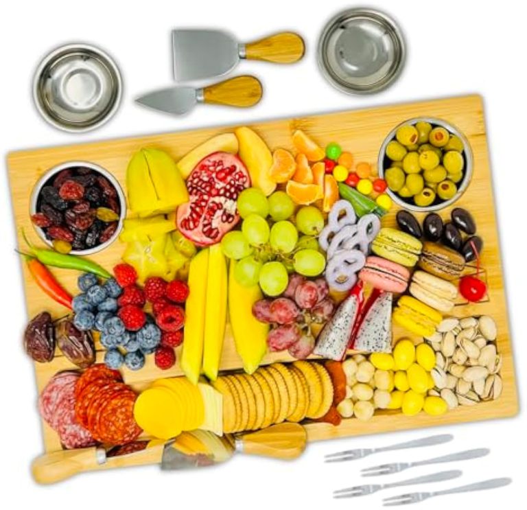 Bamboo cheese board with knives, bowls and forks arranged with cheese, fruit, crackers and small snacks