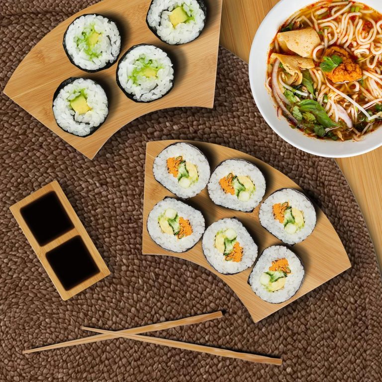 Sushi rolls served on two fan-shaped bamboo plates beside a divided sauce dish and chopsticks
