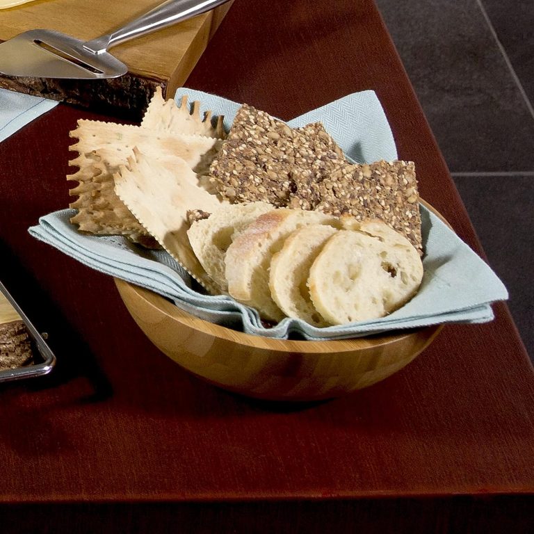 Bamboo bowl lined with a cloth and filled with sliced bread and crackers on a dining table