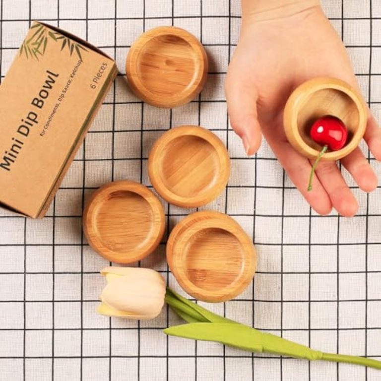 Mini bamboo sauce bowl with a cherry held in a hand beside other bowls and a six-piece box