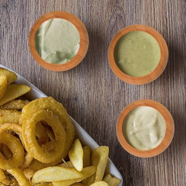 Three round bamboo dipping bowls with sauces beside fries and onion rings