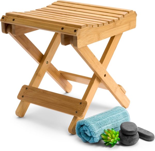 Natural bamboo folding stool with a slatted top and crossed legs beside a rolled towel and stones