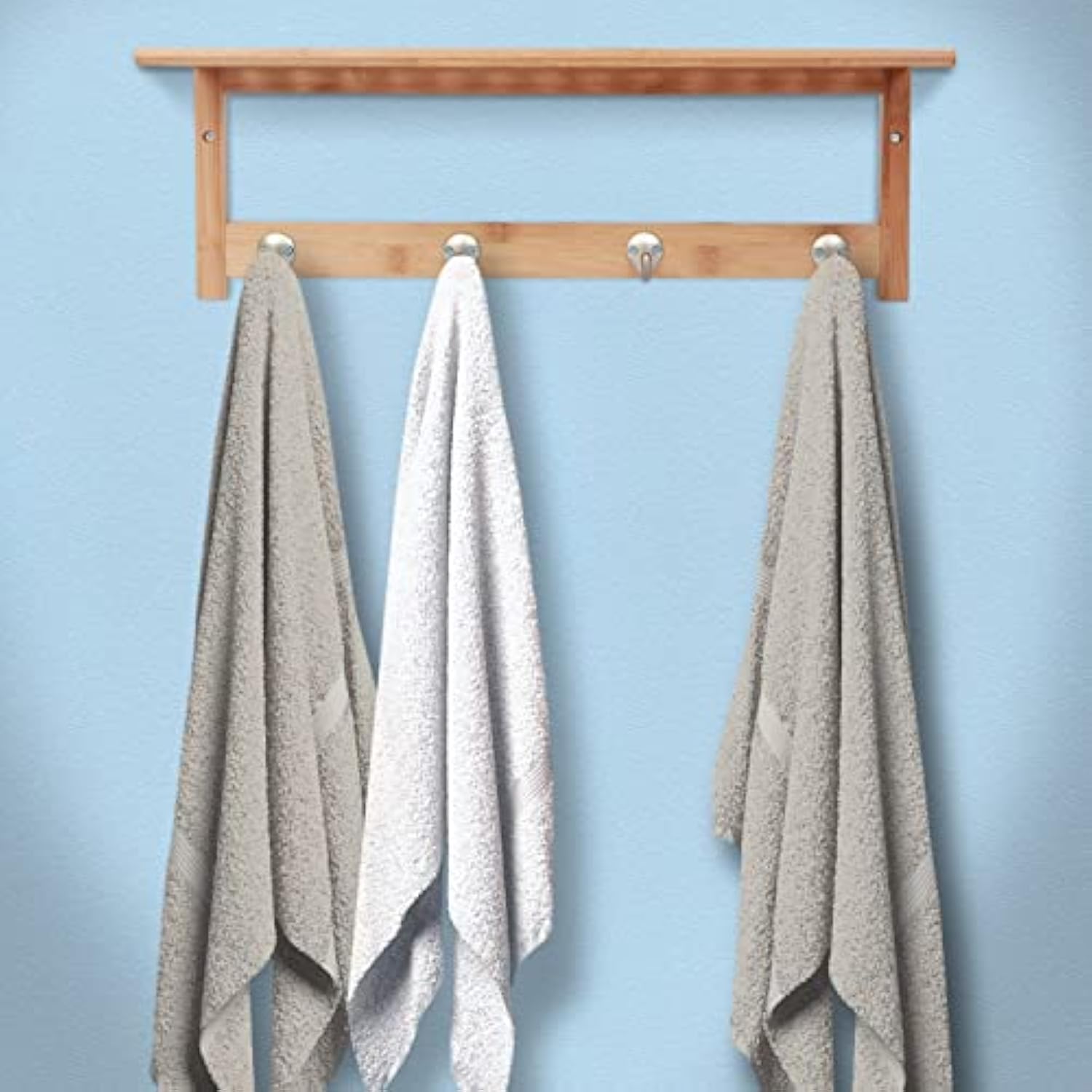 Bamboo wall shelf mounted on a blue wall with three towels hanging from its four hooks