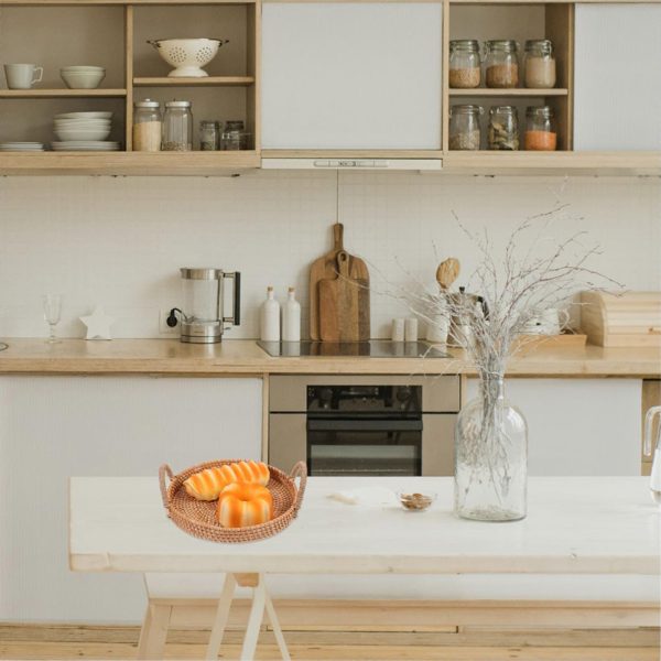 Round rattan tray with loop handles and orange decorations on a white table in a kitchen