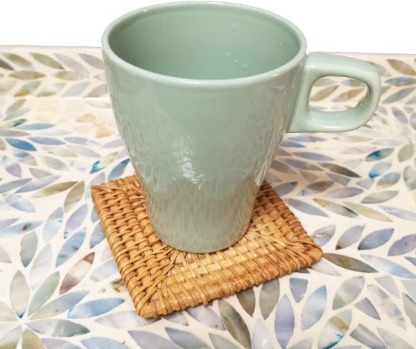 Pale green mug placed on a square woven rattan coaster on a patterned table