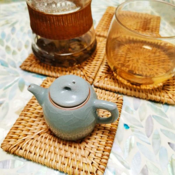 Square rattan coasters beneath two glasses and a small ceramic teapot