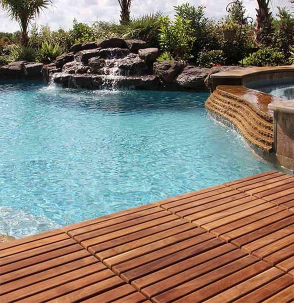 Wood floor tiles beside an outdoor swimming pool with rocks and planting