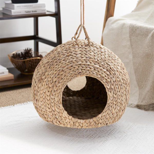 Empty woven water hyacinth cat bed cave suspended by cords with front and rear openings visible
