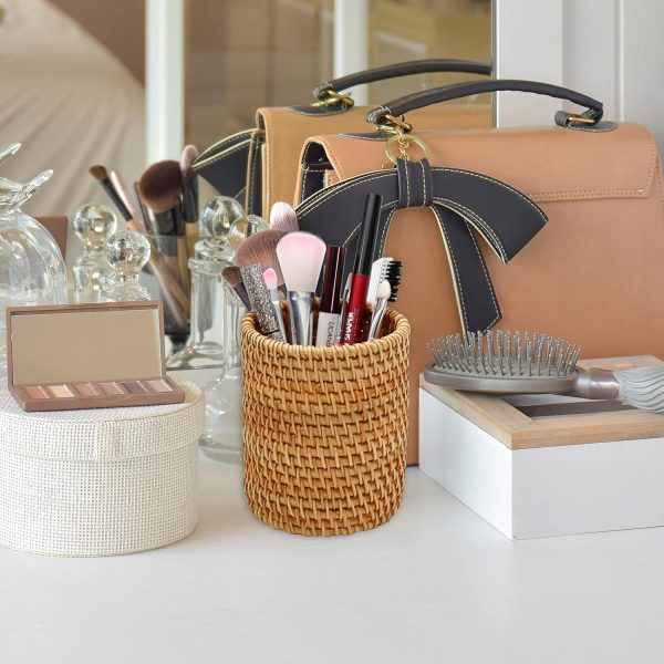 Cylindrical rattan holder displaying makeup brushes on a vanity beside a mirror and handbag
