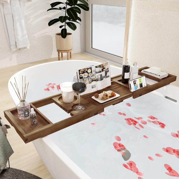 Extendable teak bathtub caddy across a white bath with book support, phone slot, glassware and bath accessories